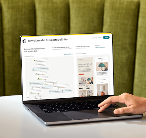 Immagine di una persona seduta a una scrivania, che guarda lo schermo di un laptop che mostra la funzionalità di revisione del percorso predefinito di Mailchimp. La funzionalità mostra l'anteprima di un percorso di automazione e una visualizzazione astratta delle interfacce e-mail e SMS del brand fittizio Assembly.